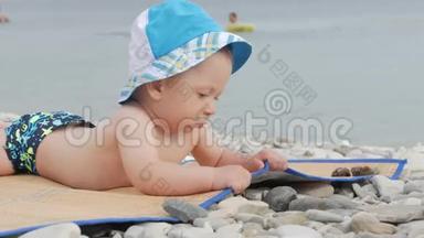 可爱的小宝宝，戴着一顶大帽子坐在海滩上微笑。